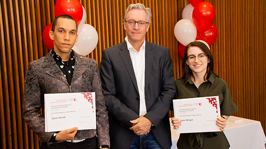 Male instructor stands between male and female students holding prize certificates while smiling for a photo