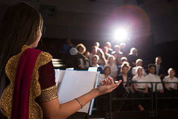 Young woman stands at podium to read a presentation in front of an audience