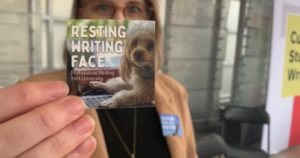 A picture of a person holding a sticker that reads "Resting Reading Face."