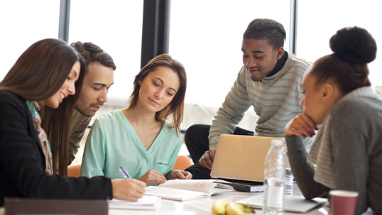 group of five diverse people at a desk while working together with notebooks open