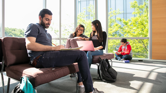 various students sit in the learning commons on the sofas and by the window