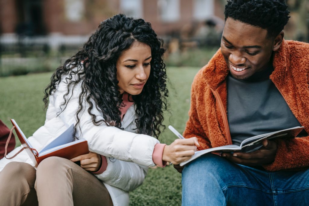 Men and Women looking at a notebook, the woman is writing in it