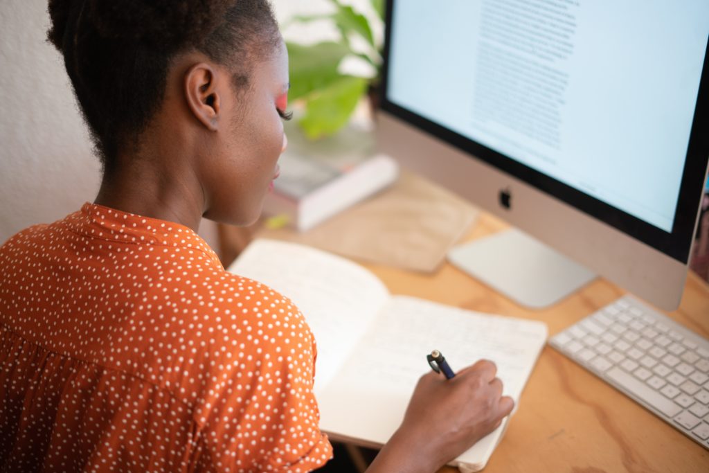 Girl writing in a notebook at a computer desk