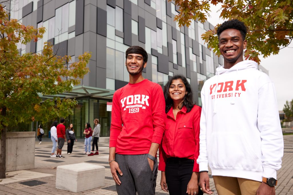 Three students wearing York sweatshirts standing outside and smiling at the camera.