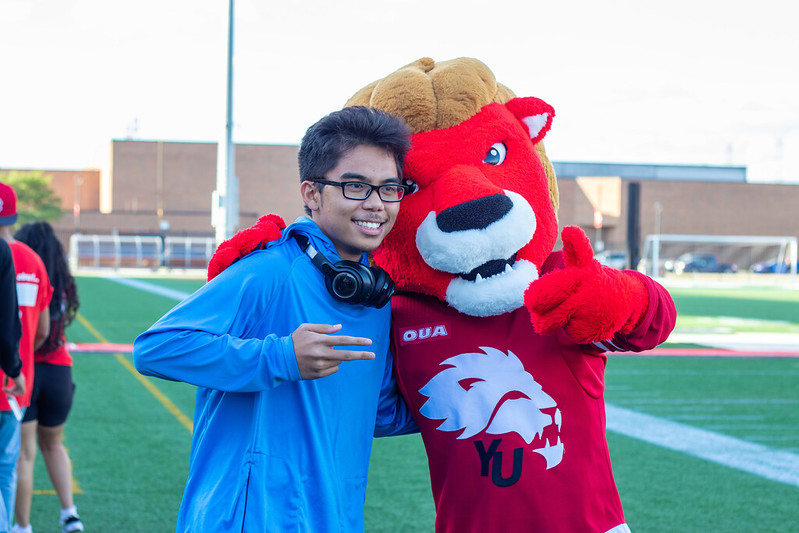 A student wearing glasses and headphones hugging the York Lions mascot.