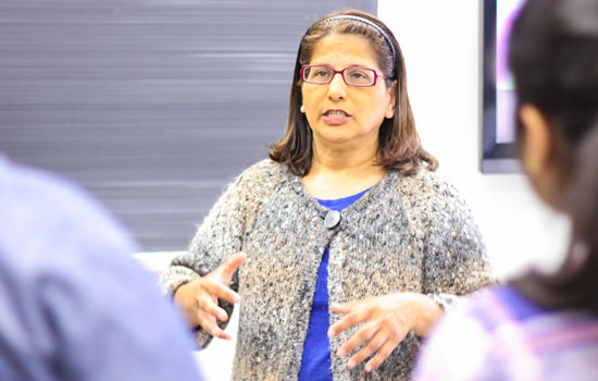 A woman stands in front of a chalk board and speaks to two other people who have their backs to the camera.