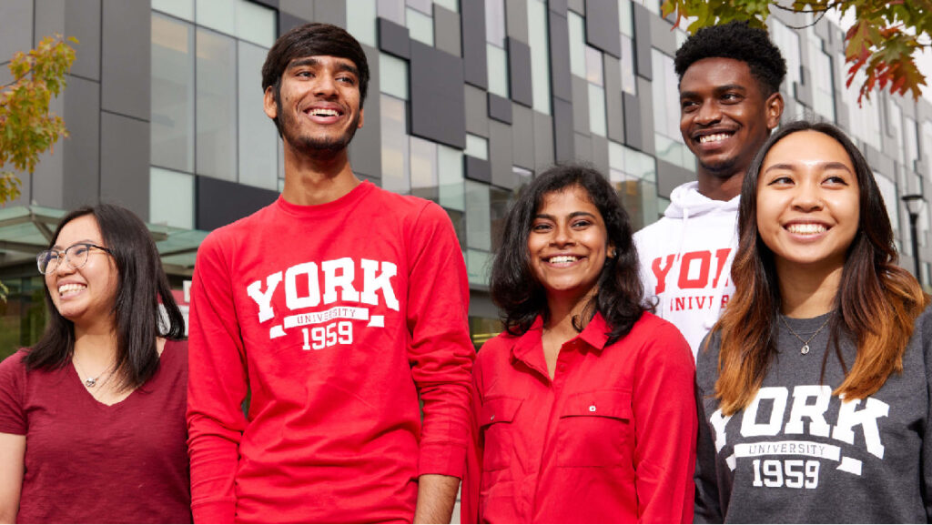 Five students dressed in York University branded clothing smile outside on a sunny day.