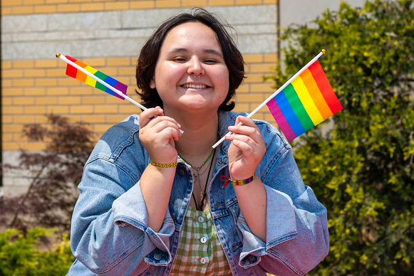 A student smiling and waving two Pride flags.