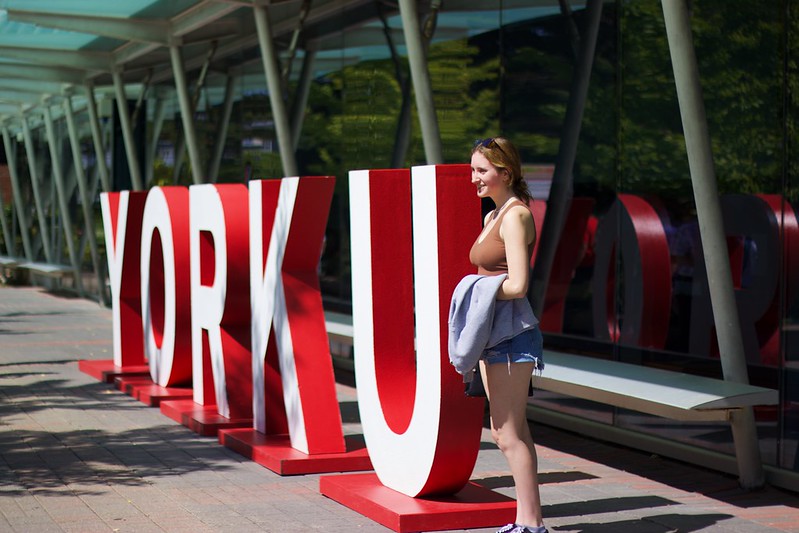 A female student poses with the giant York U sign outside at York, along the campus walk.