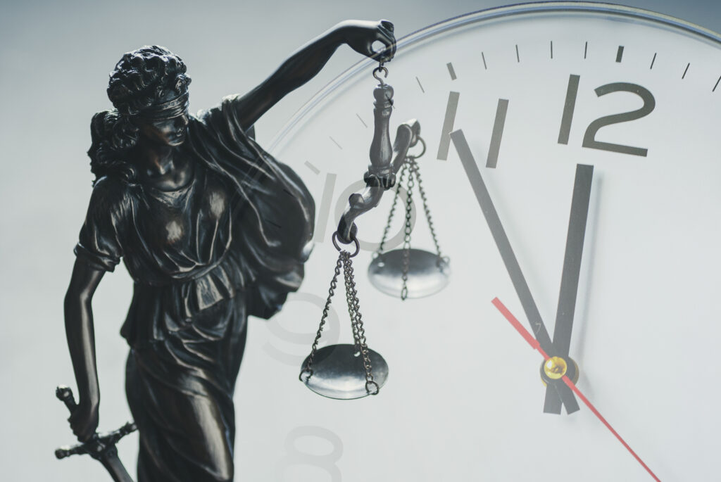Silver statuette of Justice holding the scales of justice and law enforcement in front of a clock dial in a close up conceptual composite image