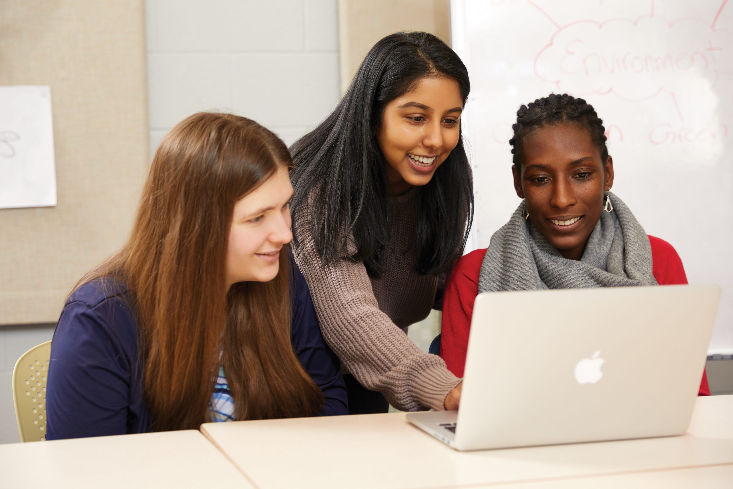 Three students looking at a laptop together