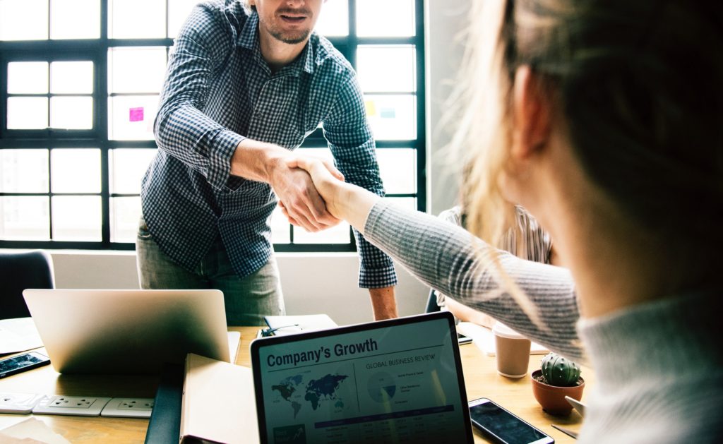 Two people with laptops shaking hands.