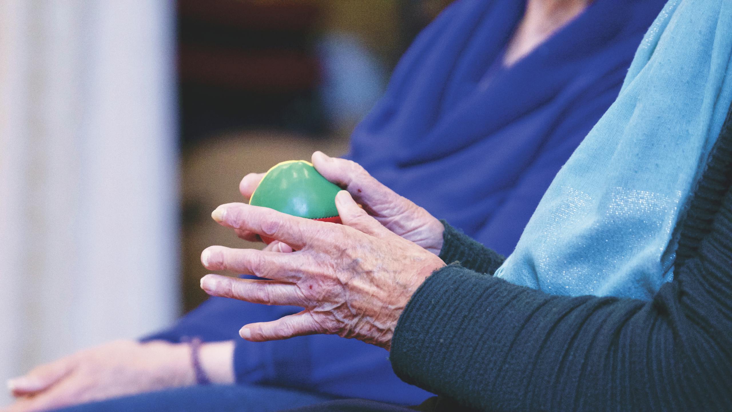 Close-up of senior person's hands holding a green therapy ball, showcasing wrinkles and care.