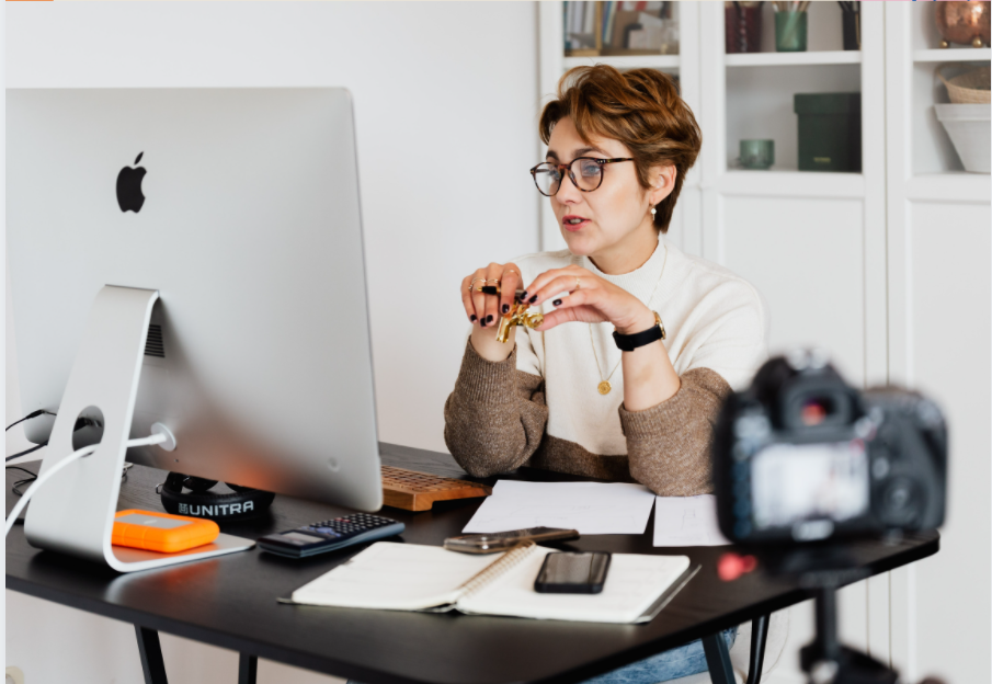 A woman speaking in front of a camera and her computer.