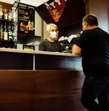 A person talking to a bartender who is wearing a mask.