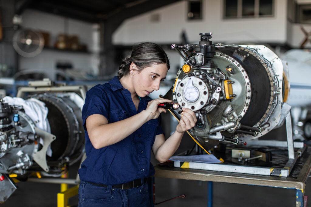 Real-life image of a young female aircraft engineer apprentice at work, showcasing strength and expertise in avionics