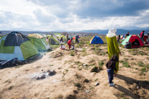 An image of a refugee camp with men, children, and women in the distance. 