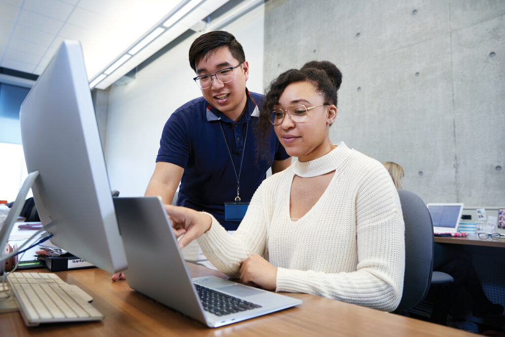 A staff member assists a student at a computer.