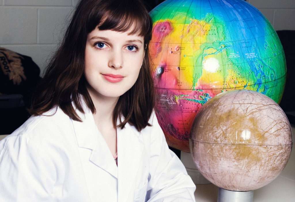 Female student beside world globe and holding another globe.