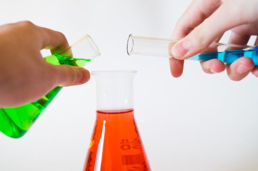 Two hands of person holding and pouring liquid in Chemistry lab.