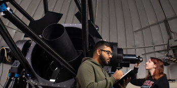 Two students at the York U Observatory, one is taking notes, one is looking through the telescope