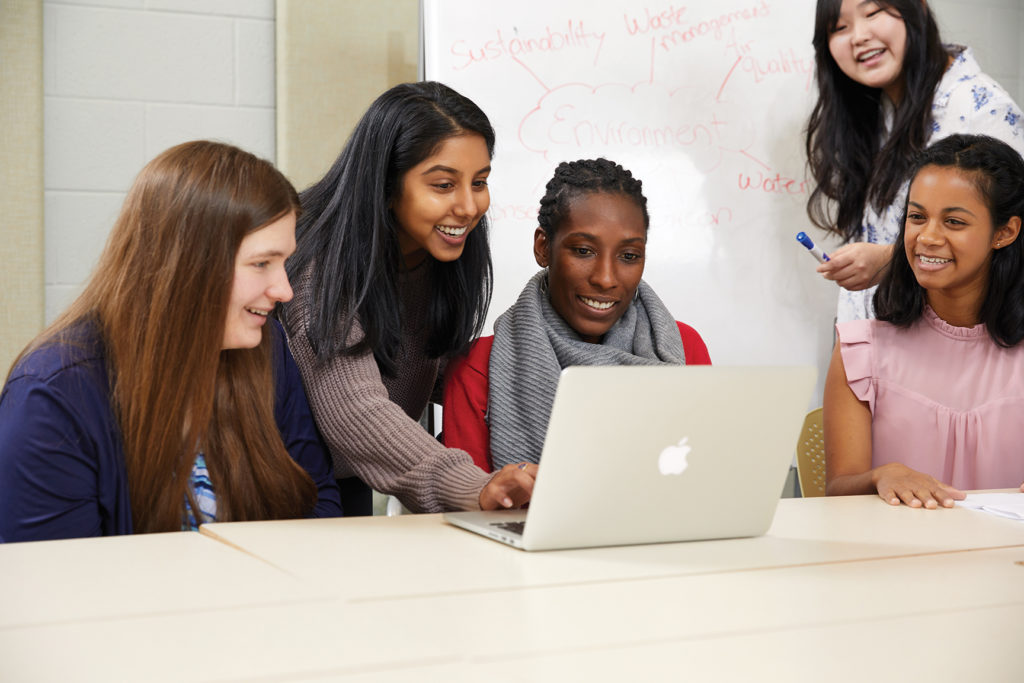 Group of female students looking at shared computer.