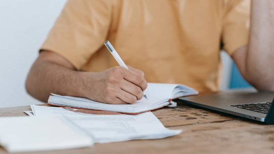 person writing in a notebook next to laptop