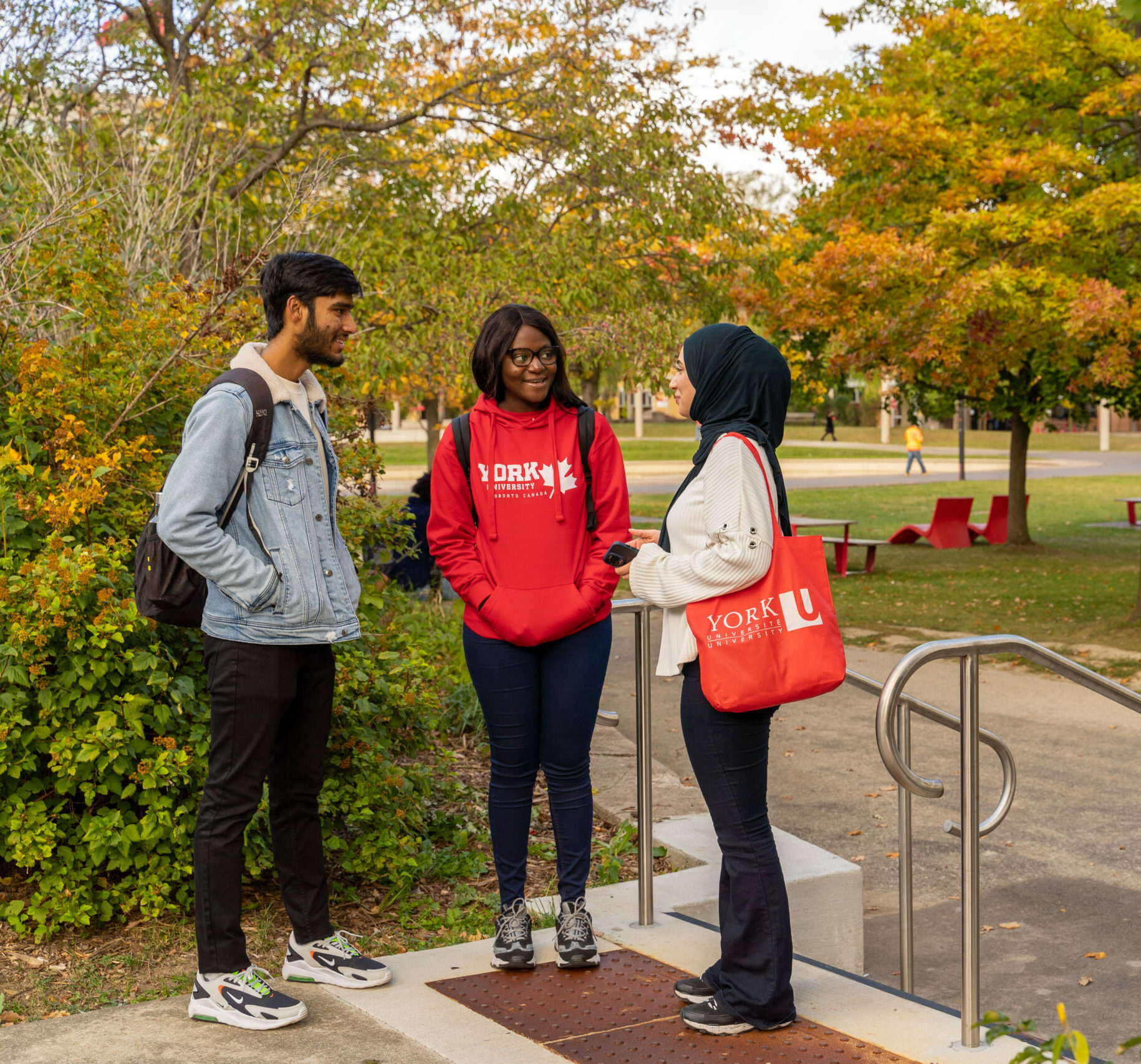 Three students speaking happily with each other next to a garden.