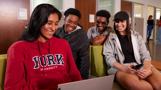 Four students laughing looking at a laptop