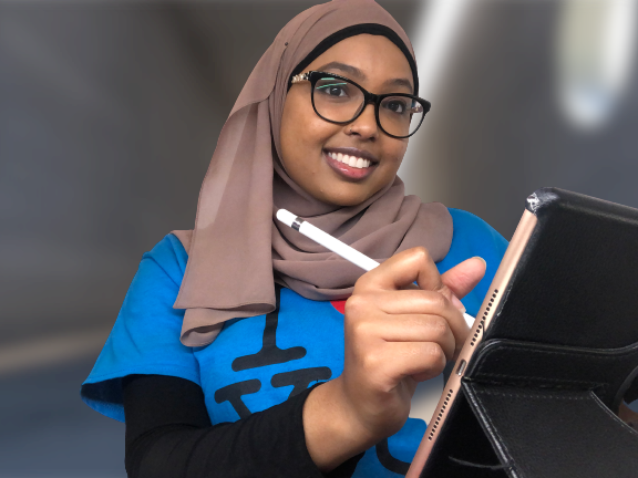 A Learning Skills Service Peer wearing their blue uniform t-shirt holds a tablet and smiles.