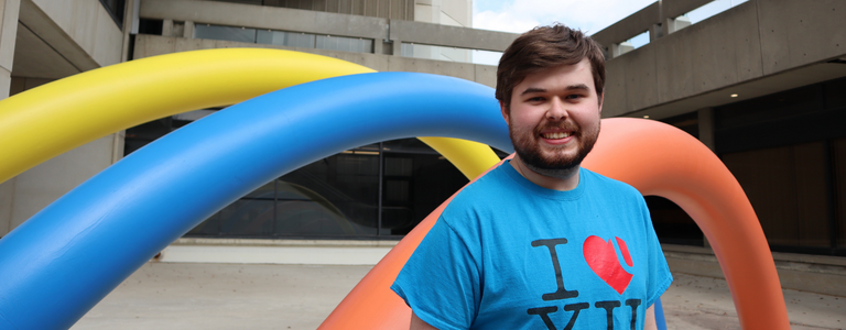 A Learning Skills Peer stands outside with a rainbow sculpture in the background, just outside of Scott Library.