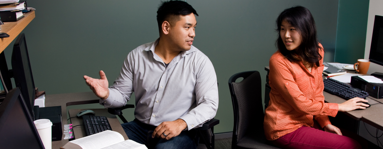 Two people sitting at desks turn and face each other to have a conversation.