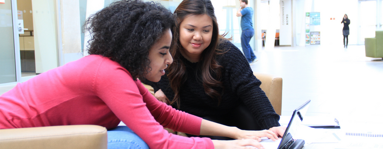 Two students study together using the same laptop and smiling.