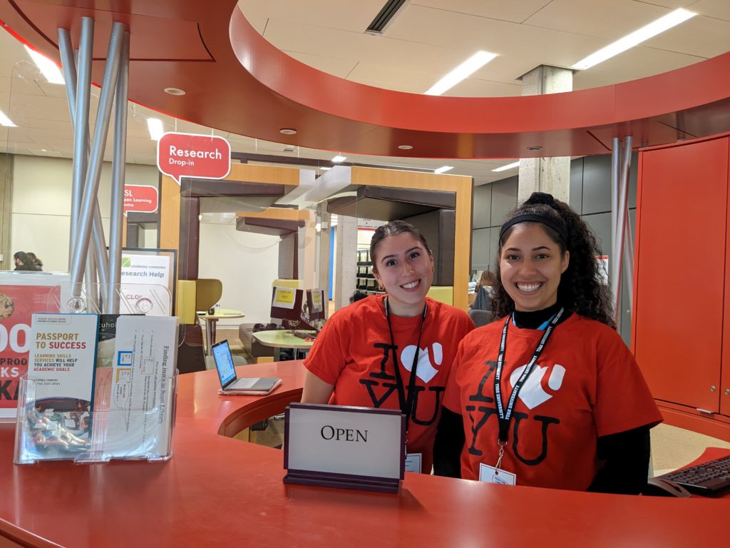 Two Learning Skills Peers stand at the red welcome desk on the second floor of Scott Library. 