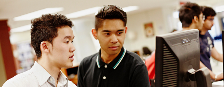 Two students work together on the same computer monitor.