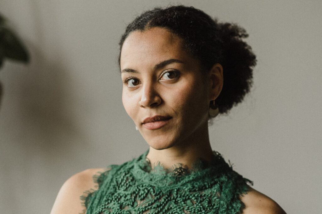 Sara Yacobi-Harris - portrait photo with hair tied back, wearing a green dress in front of a blurred background.