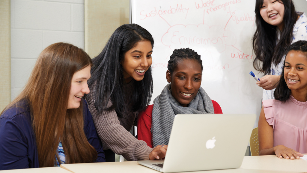 A group of five students huddle around a laptop on a table top at the York University Learning Commons.