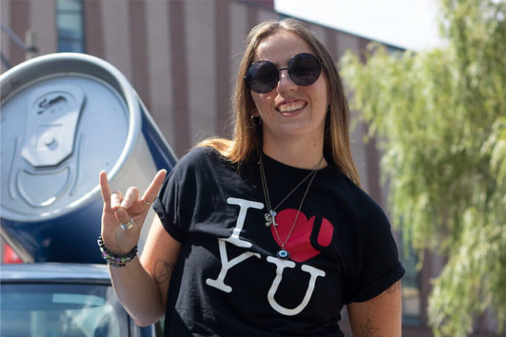 A girl wearing sunglasses and an "I Heart YU" logo t-shirt smiles in the summer sun in the York Commons.