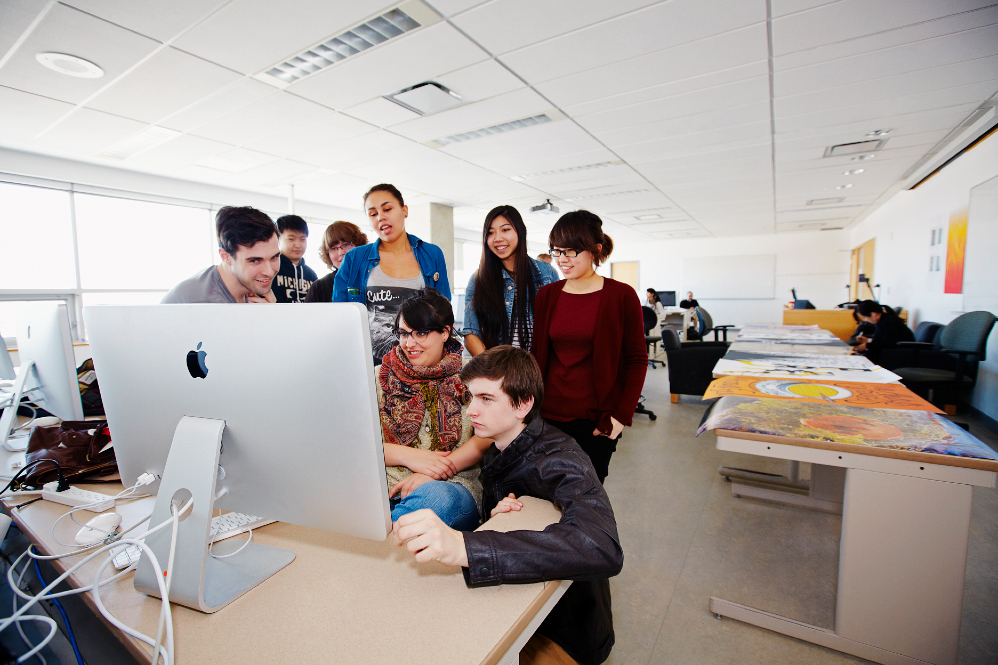 Group of students gathered around a computer. 
