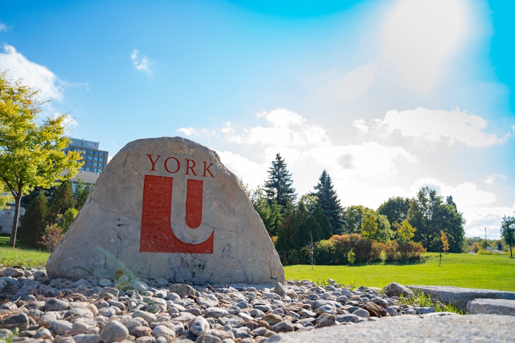 Image of York University campus. Large rock with York insignia with small stones in foreground. 