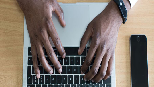 Black male hands typing on a laptop keyboard. 