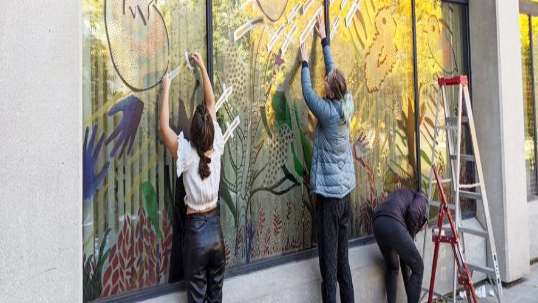 Students working on a window art mural called For the Birds.