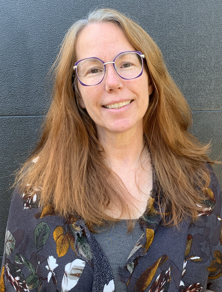 Dr. Carolyn Steele smiling at the camera, standing in front of a grey background