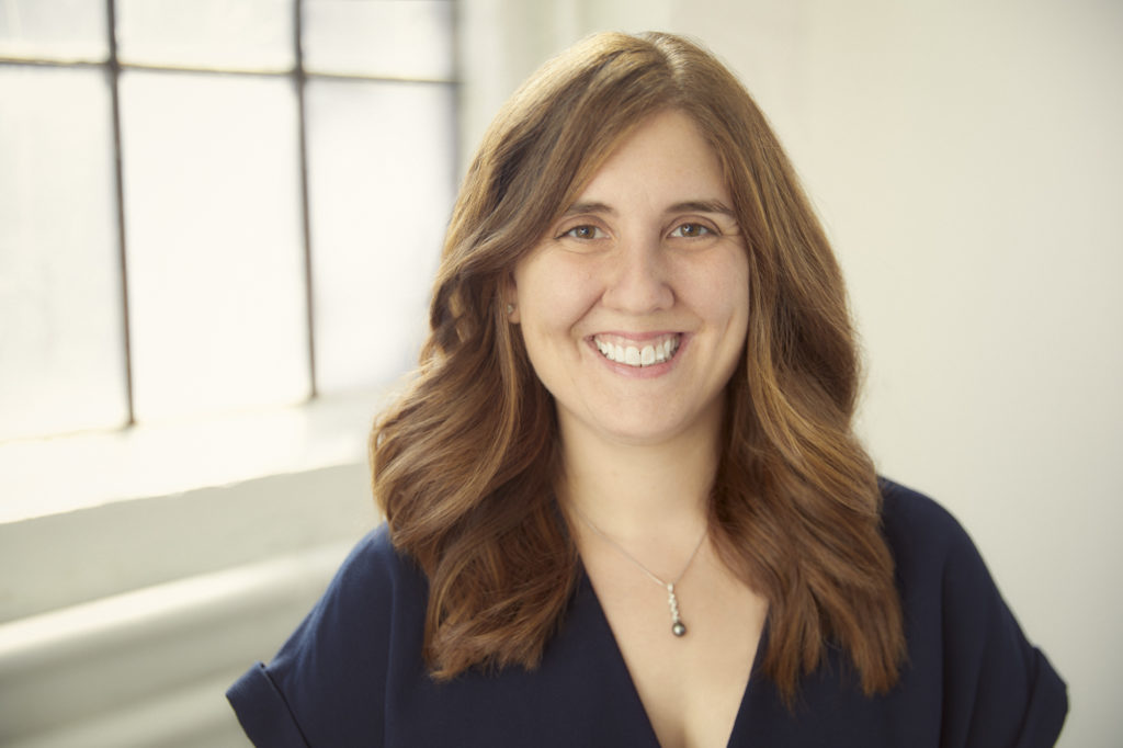 Ashley Nahornick, an individual with long, brown hair, wearing a blue blouse, smiling into the camera