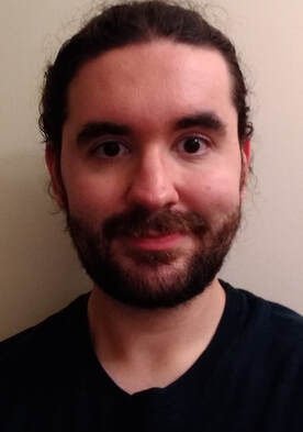 Dr. Andrew Molas, an individual with dark brown hair and a full beard, wearing a black t-shirt, smiling into the camera.