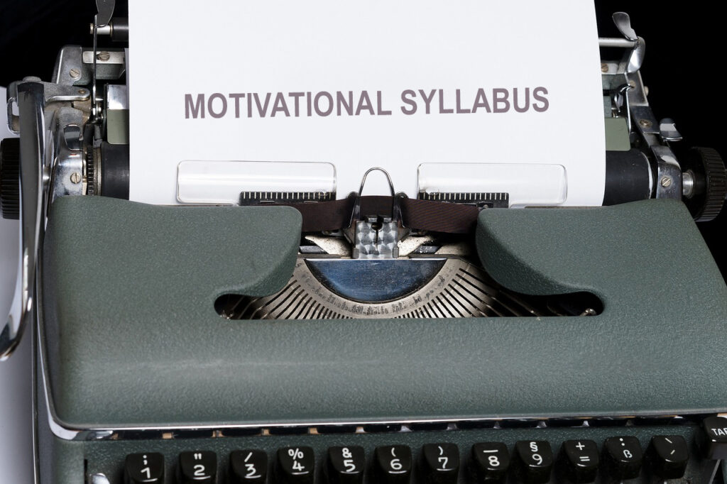 An old grey typewriter is churning out a sheet of paper with the words 'Motivational Syllabus' typed at the top. Purpose of the image is to illustrate the concept.
