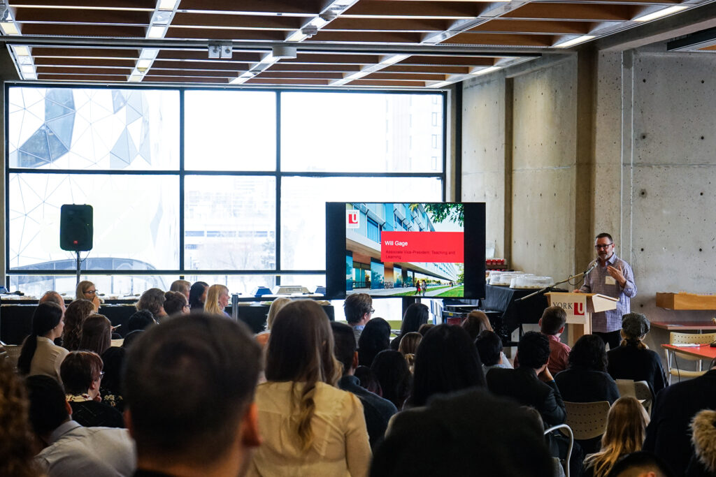 event presentation with speaker at a podium with a screen of visuals