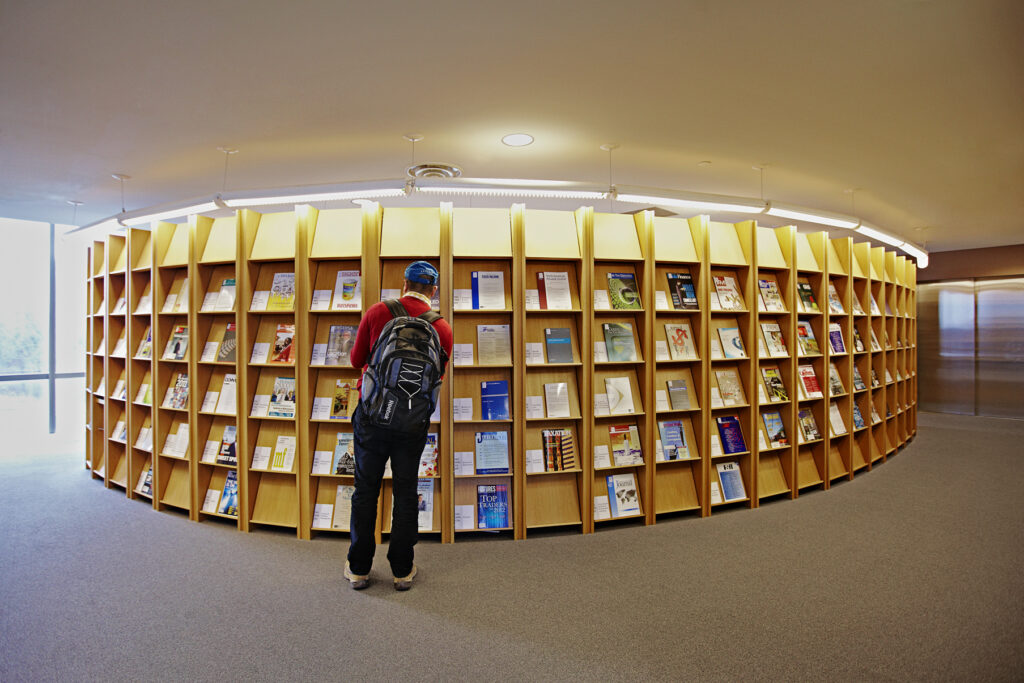 a student with a backpack browsing a large collection of journals on shelves in a library.