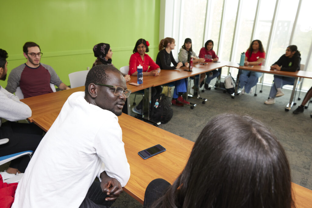 An active seminar where students are connecting with each other in discussion with deks arranged in a U shape