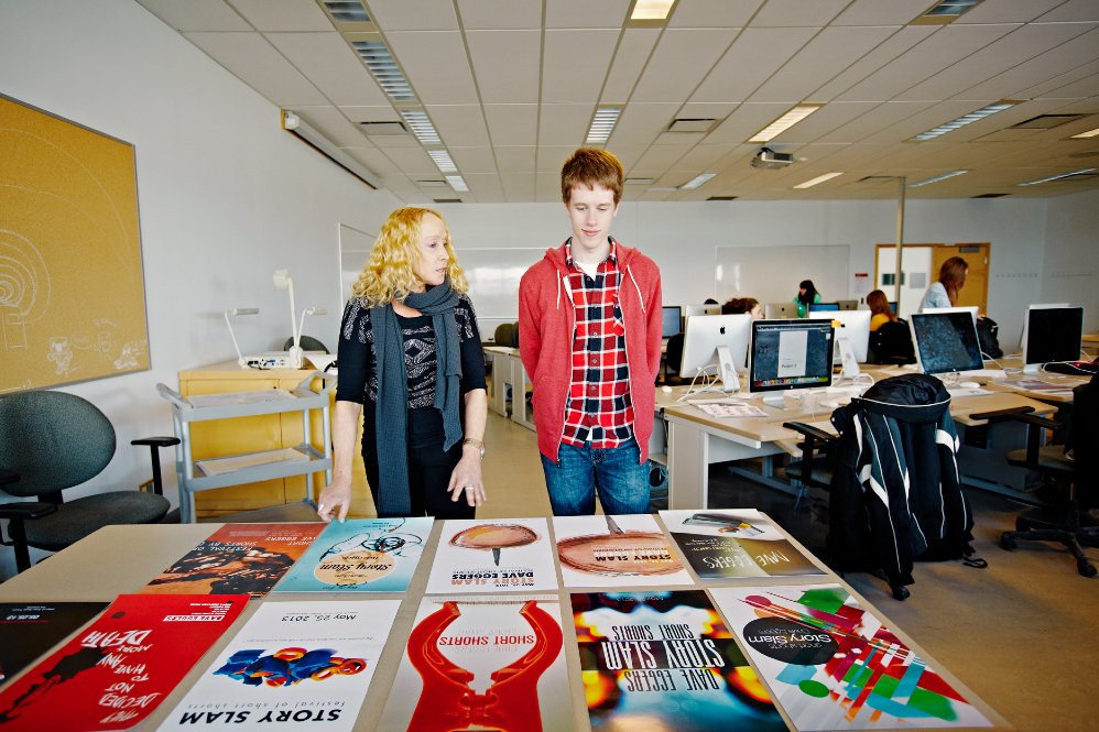 An instructor facing a student in front of colourful pages arranged on a table.